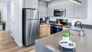 A modern kitchen with stainless steel appliances, wooden cabinets, and a central island with a sink and decorative items. - Sugarhouse! Mountain View 3BR, 2BA Gym, Parking (Salt Lake City)