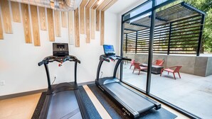 A modern fitness room with two treadmills, a digital display, and a view of outdoor seating. - Sugarhouse! Mountain View 3BR, 2BA Gym, Parking (Salt Lake City)