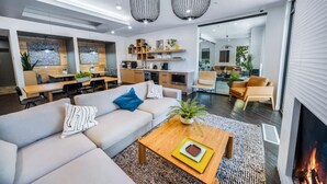 A modern living room with a sofa, coffee table, and fireplace. There is a kitchen area with a dining table and chairs, and a seating area with a couch and chairs. - Sugarhouse! Mountain View 3BR, 2BA Gym, Parking (Salt Lake City)
