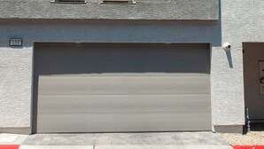 Un bâtiment moderne à deux étages, doté d’une porte de garage, d’une petite fenêtre et d’une caméra de surveillance.