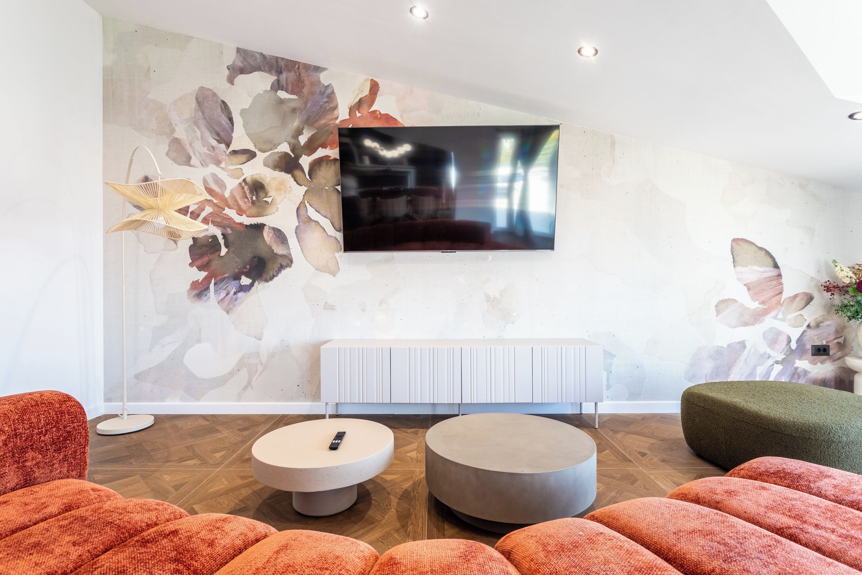 A modern living room with a flat-screen TV mounted on the wall, a white radiator below, and a large abstract painting on the wall.