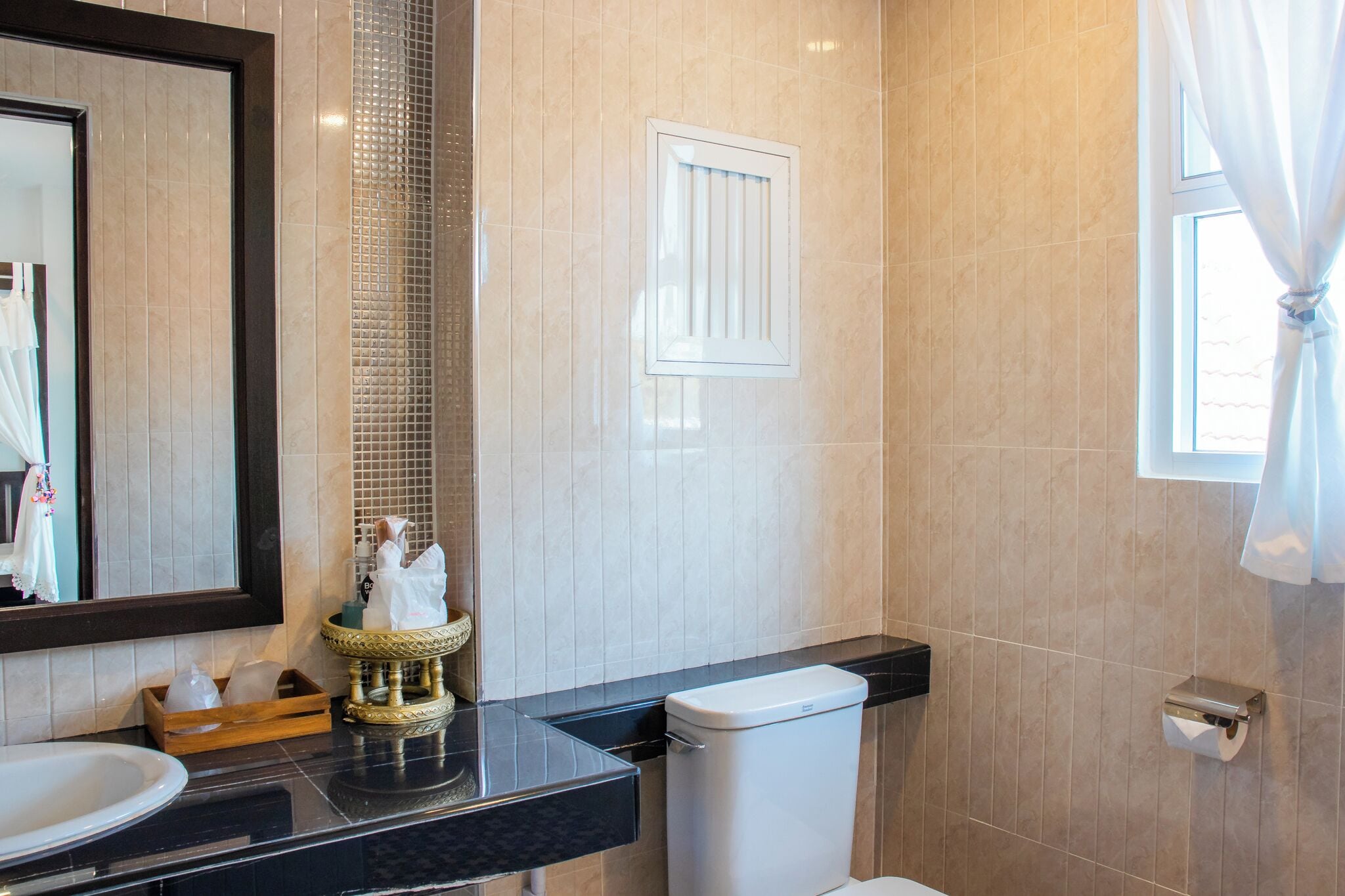 A bathroom with a large mirror, a sink, a toilet, and a window with curtains.