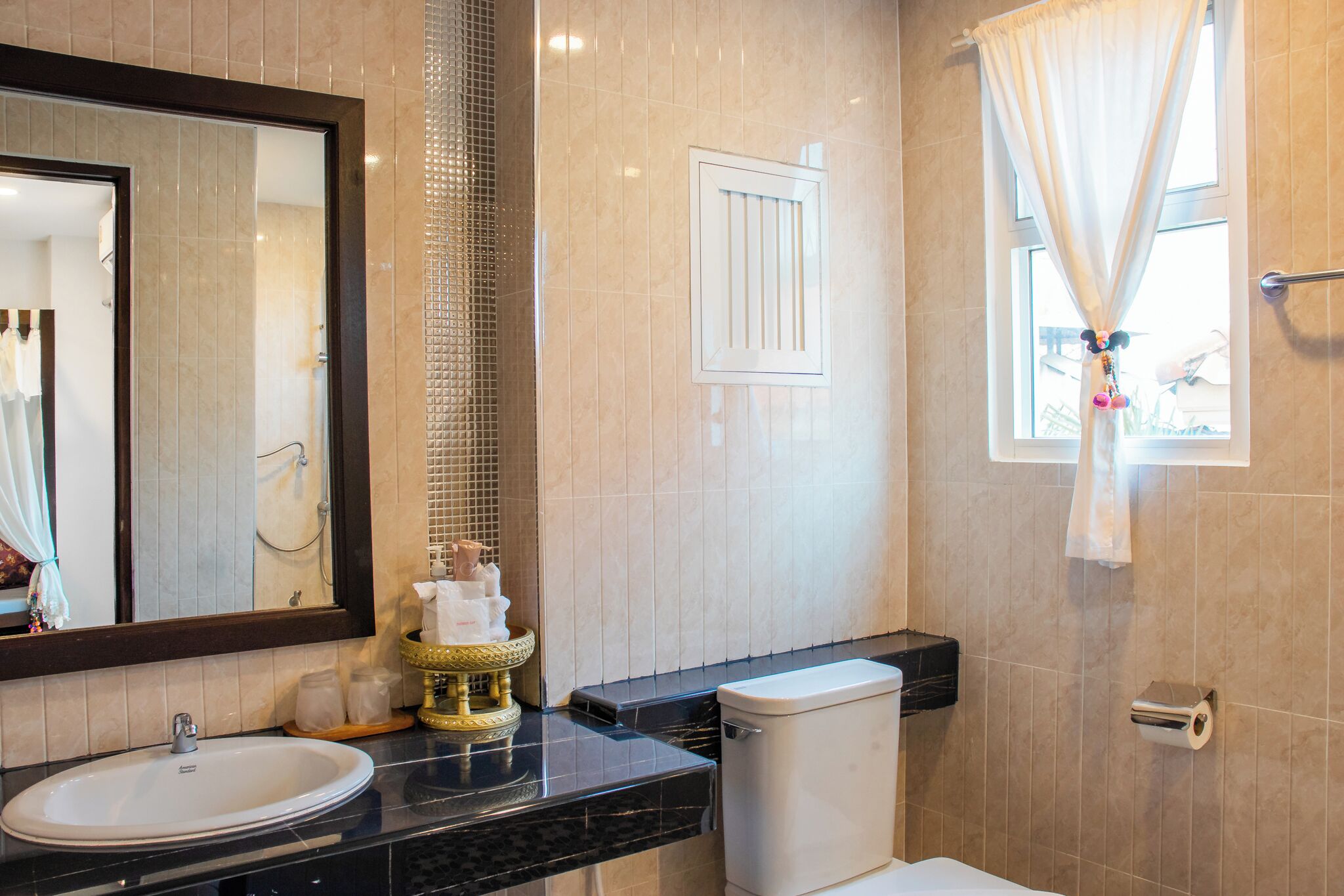 Un baño con lavamanos, inodoro y ventana con cortinas.
