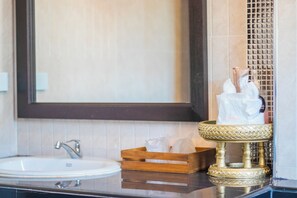 A bathroom with a white sink, a mirror, and a decorative gold basin with toiletries.