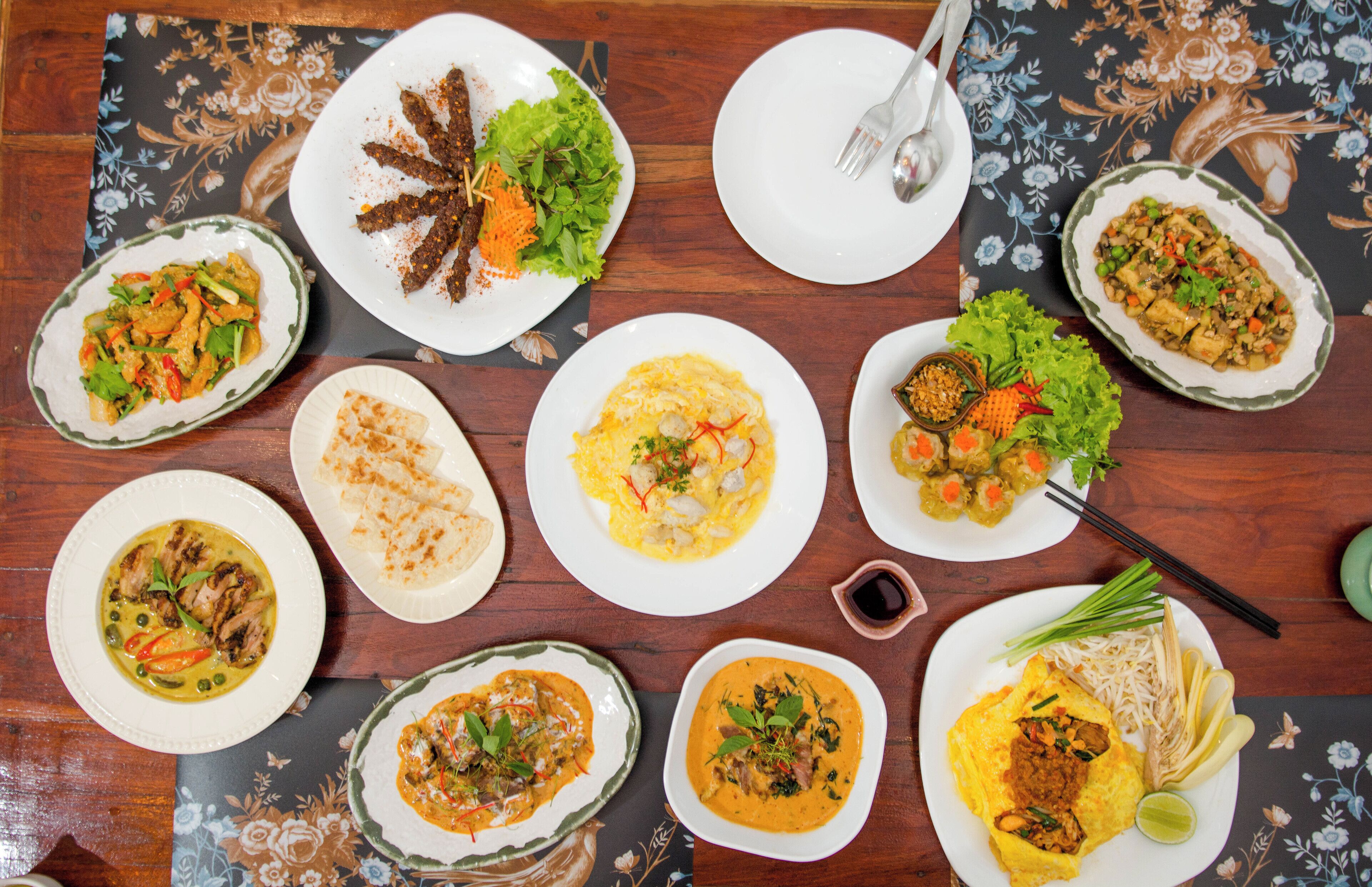 A table with various dishes including a salad, a plate of fried meat, and several bowls of soup.