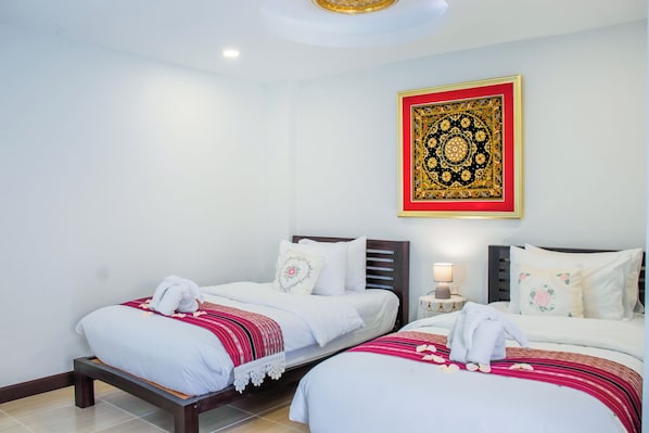A hotel room with two single beds, a nightstand with a lamp, and a decorative wall hanging. - Aba Village hotel (Chiang Mai)