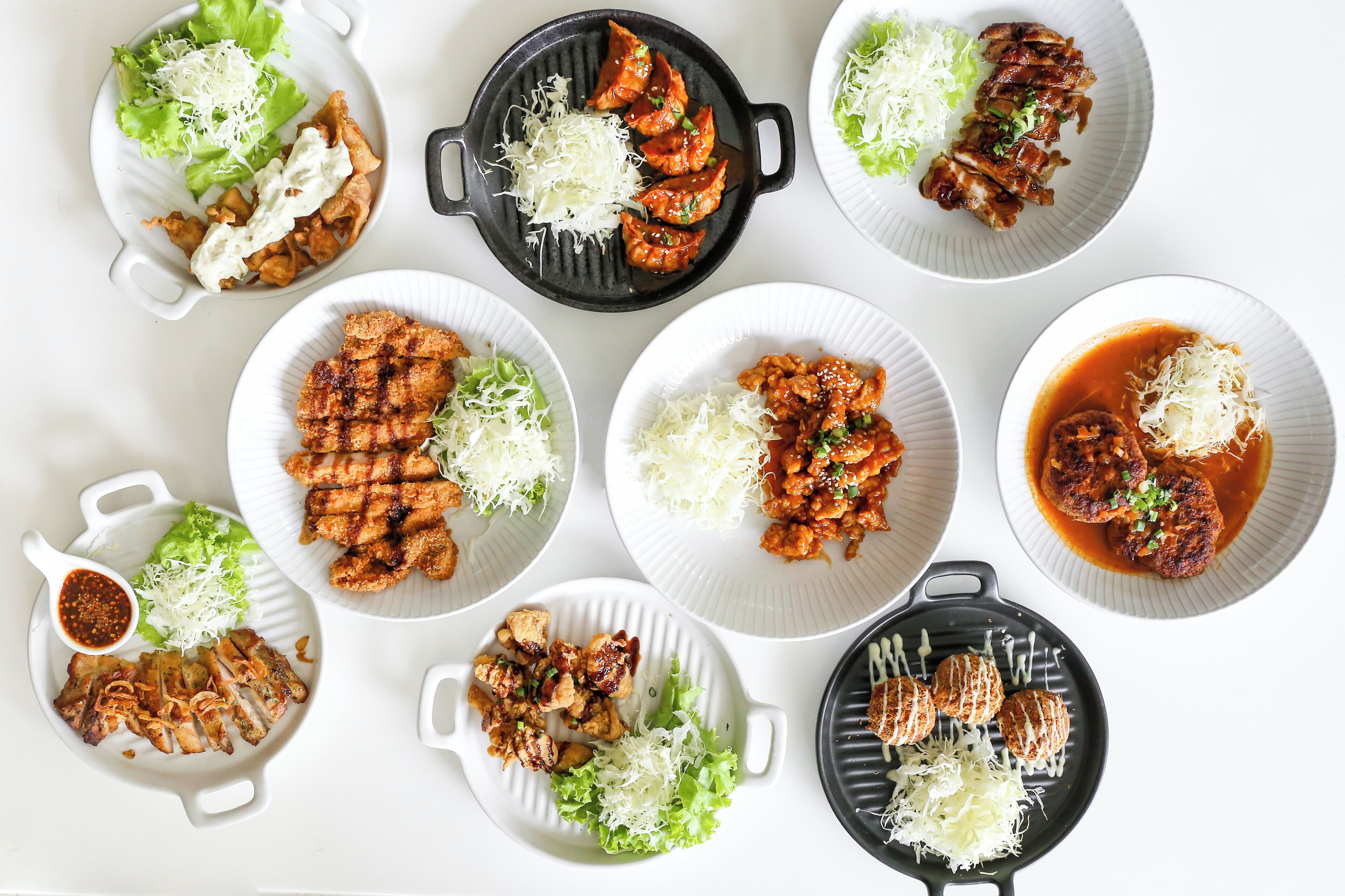 A variety of dishes including grilled meats, vegetables, and sauces, arranged on multiple plates and a grill pan.