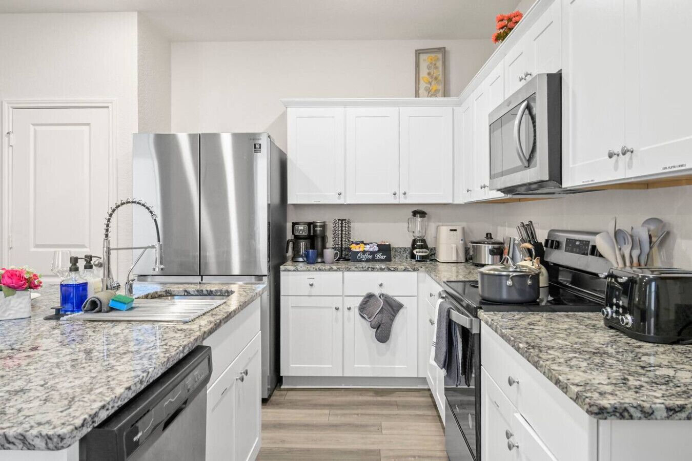 A modern kitchen with white cabinets, stainless steel appliances, granite countertops, and a coffee station.