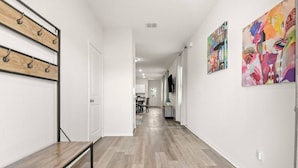A hallway with a bench, wooden flooring, and a dining area in the distance.
