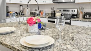 A kitchen with granite countertops, white cabinets, a stainless steel range hood, and a microwave above the stove.