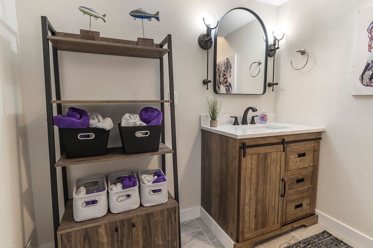 Une salle de bain avec un meuble-lavabo en bois, une étagère avec des paniers de rangement, un miroir et une petite plante.