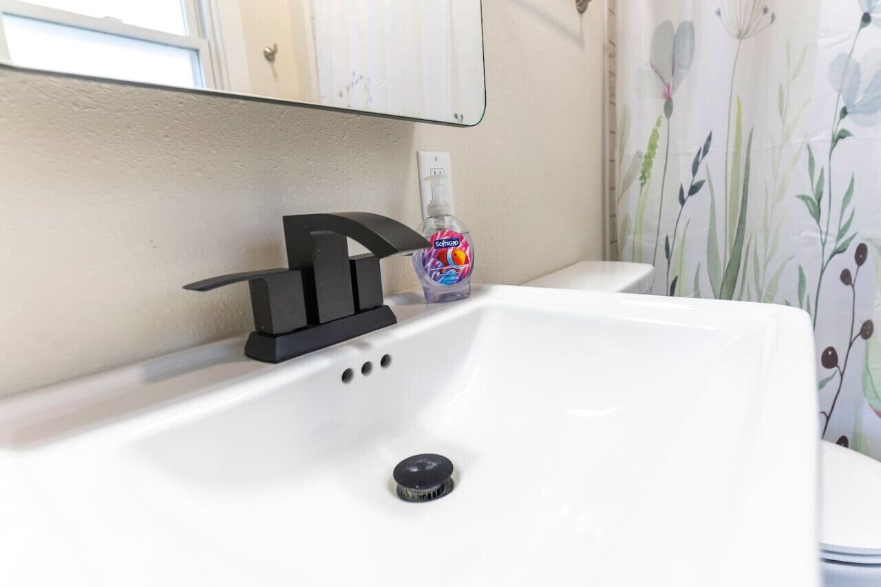 A bathroom sink with a modern faucet, a bottle of hand soap, and a mirror above it.