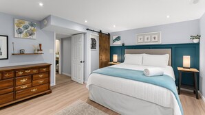Un dormitorio con cama, cómoda, mesitas de noche y una puerta que da a otra habitación.