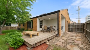 Un patio moderno con deck de madera, una mesa y sillas, y un sendero de piedra.
