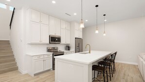 A modern kitchen with white cabinetry, stainless steel appliances, and a central island with bar stools. - GREAT LOCATION  Beautiful 2-bedroom house in Mission (Mission)