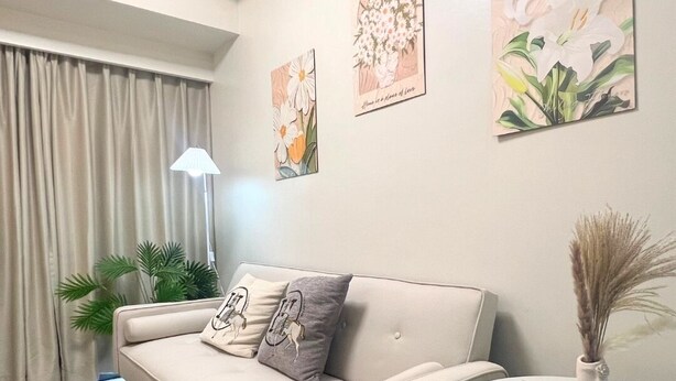Uma sala de estar moderna com um sofá bege, uma mesinha redonda e três quadros florais na parede.