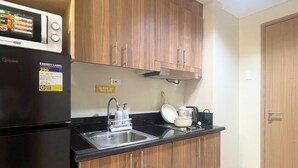 Uma cozinha compacta com armários de madeira, bancada preta, pia de aço inoxidável e micro-ondas.
