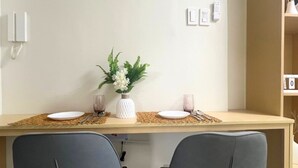 Uma área de refeições com uma mesa de madeira, duas cadeiras cinzas, um vaso branco com flores e um jogo americano trançado.