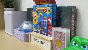 Ett skrivbord med ett Connect 4-spel, ett Scrabble-spel, en domino-uppsättning, ett ställ för Scrabble-brickor och en grön leksaksgroda.