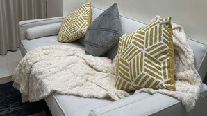 En vit soffa med ett mjukt, vitt överkast, tre mönstrade kuddar och en mörk matta.