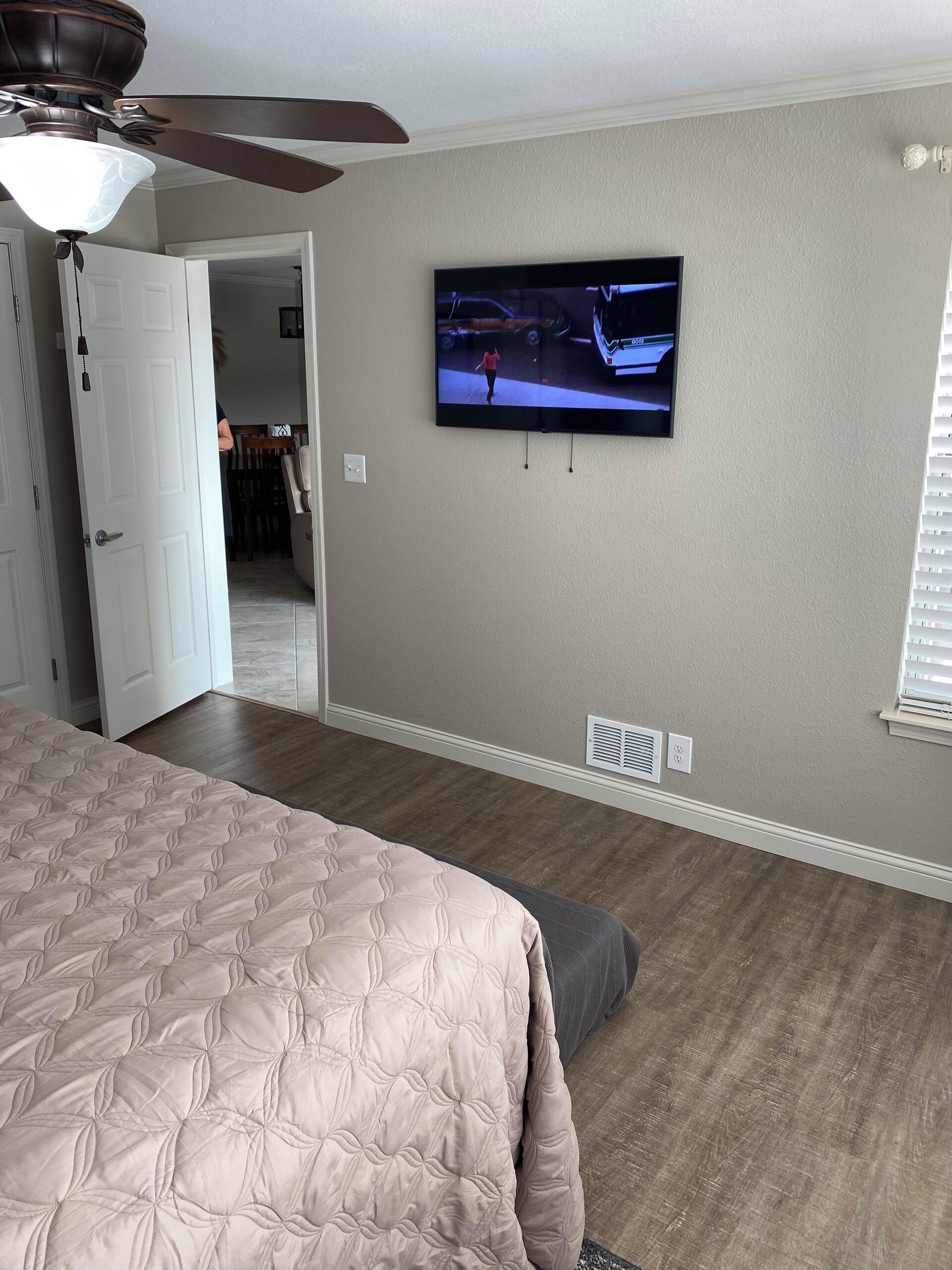 A bedroom with a bed, a ceiling fan, a TV on the wall, and a door leading to another room.