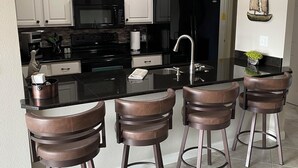 A modern kitchen with white cabinets, a black refrigerator, a stainless steel sink, and four bar stools. - Stunning, updated lakefront 2-bedroom condo.  14x40 boat slip available for rent (Osage Beach)