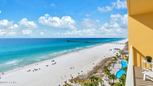 Blick auf einen Strand mit einem Steg, der ins Meer führt, sowie ein Sandstrand und ein Poolbereich.