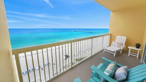 Ein Balkon mit Blick auf Strand und Meer, weiße Liegestühle und ein Tisch mit einer Pflanze.