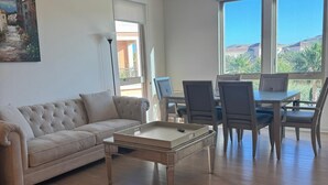 Ein geräumiges Wohnzimmer mit einem beigefarbenen Sofa, einem Couchtisch und einem Essbereich mit Stühlen und einem Tisch.