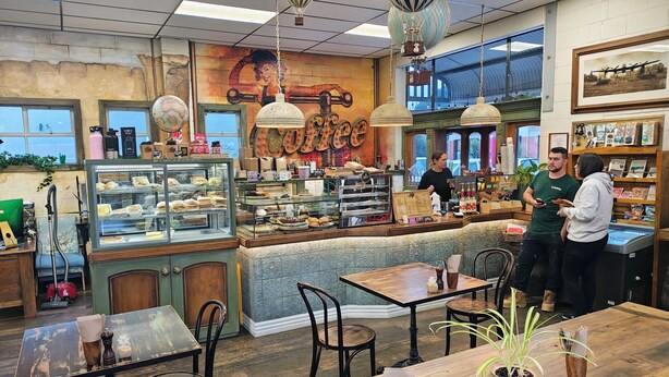 A cozy café with a vintage interior, featuring a counter with a menu, a display case with pastries, and a seating area with tables and chairs. - Central Lofts Unit 1 (Queenstown)