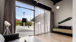 A modern hotel room with a large sliding glass door, a sofa, a coffee table, and a skateboard on the wall. - Central Lofts Unit 1 (Queenstown)