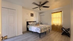 Ein Schlafzimmer mit Bett, Deckenventilator, Fenster mit Vorhängen und einer Tür.