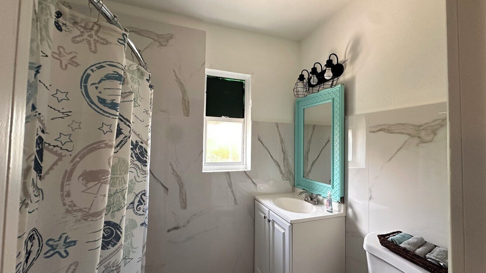 Une salle de bain avec un rideau de douche orné d’un motif sur le thème de l’espace, une fenêtre au-dessus du lavabo et un miroir avec un cadre turquoise.