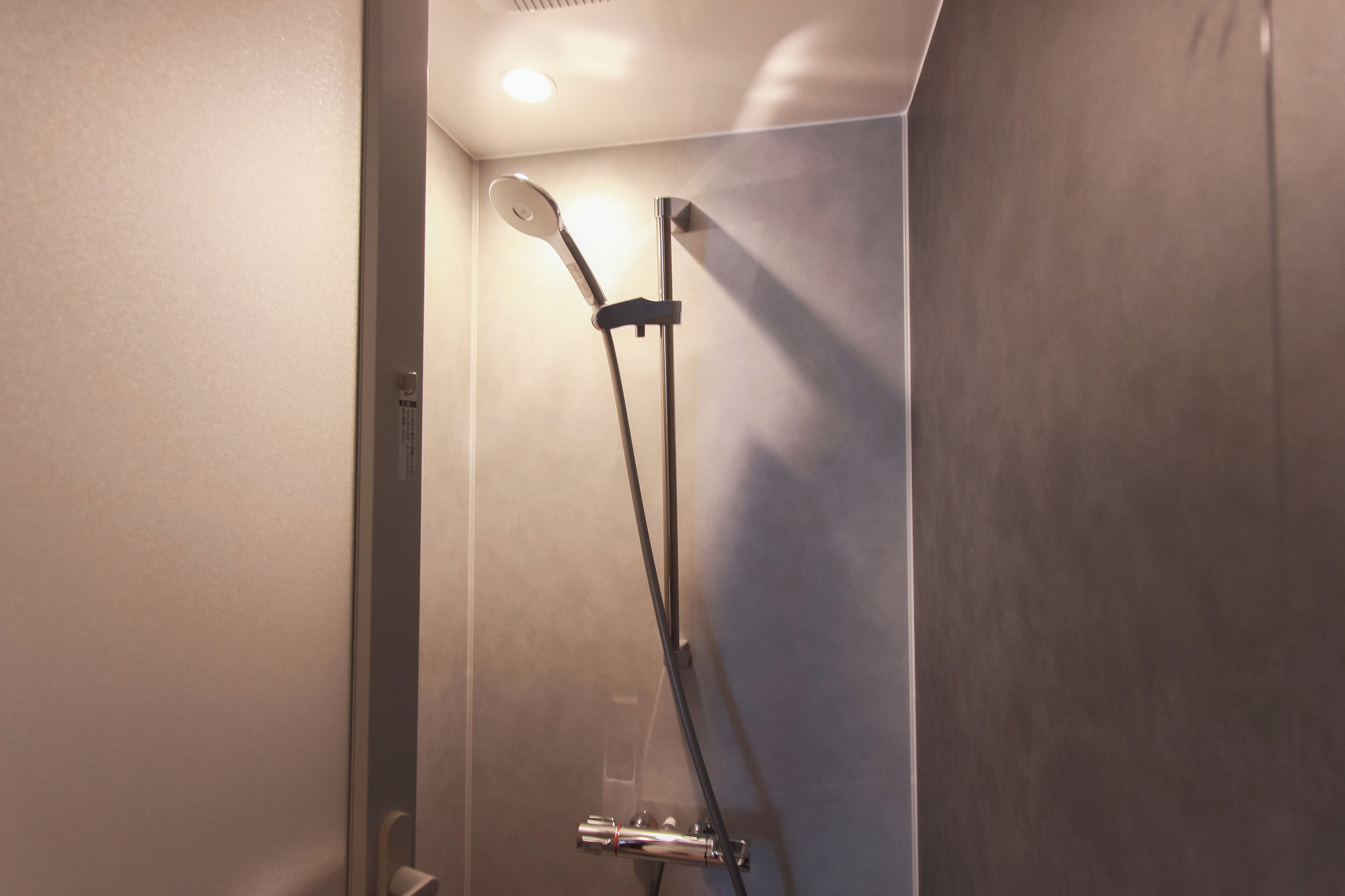 A shower with a handheld showerhead and a wall-mounted control panel.