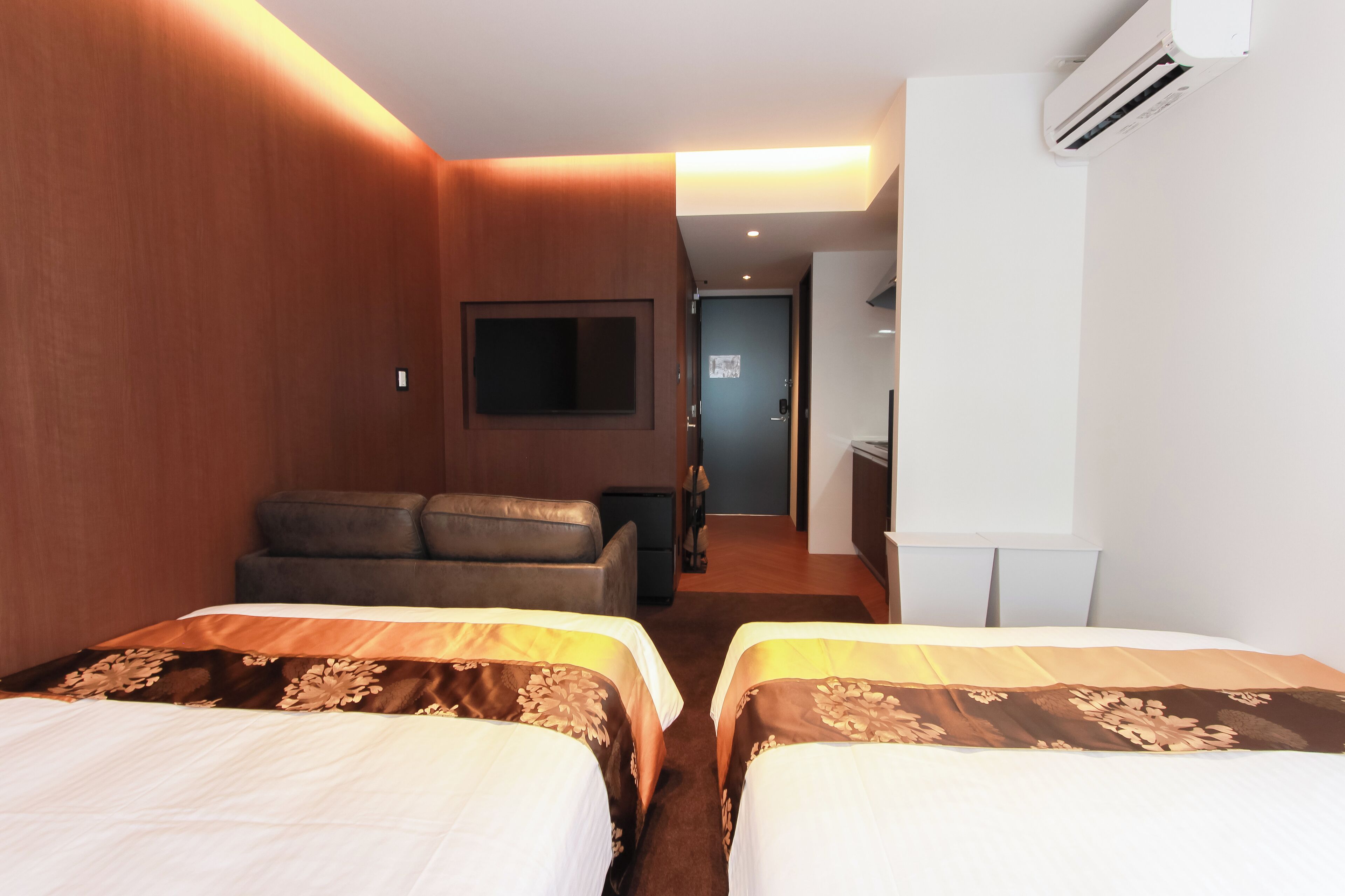 Une chambre d’hôtel avec deux lits, un canapé, un téléviseur à écran plat et un appareil de climatisation.