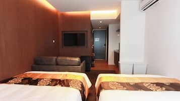 A hotel room with two beds, a sofa, a flat-screen TV, and an air conditioning unit.