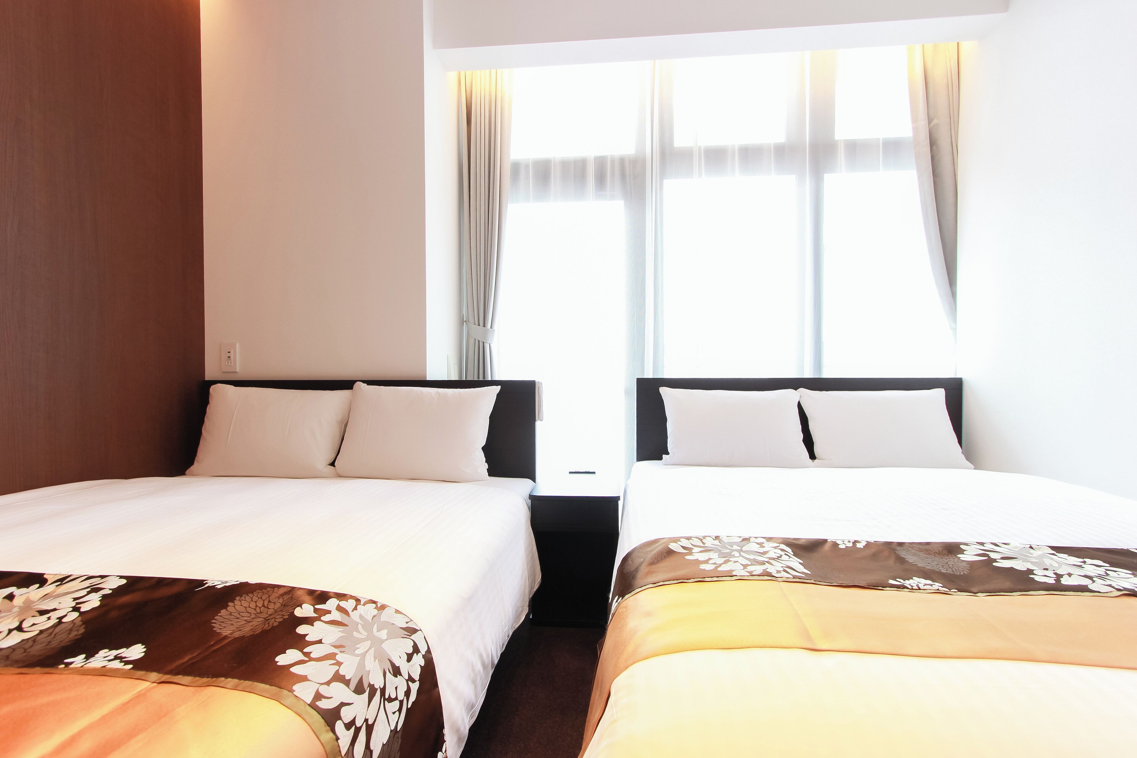 Ein Hotelzimmer mit zwei Einzelbetten, einem Nachttisch dazwischen und einem Fenster mit Vorhängen.