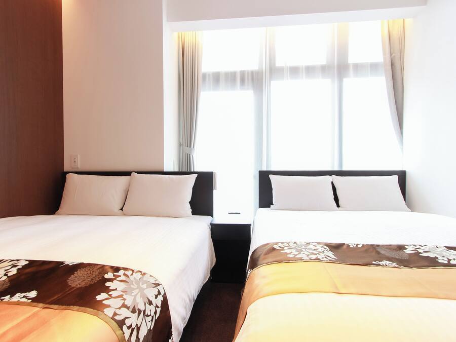 Ein Hotelzimmer mit zwei Einzelbetten, einem Nachttisch dazwischen und einem Fenster mit Vorhängen.