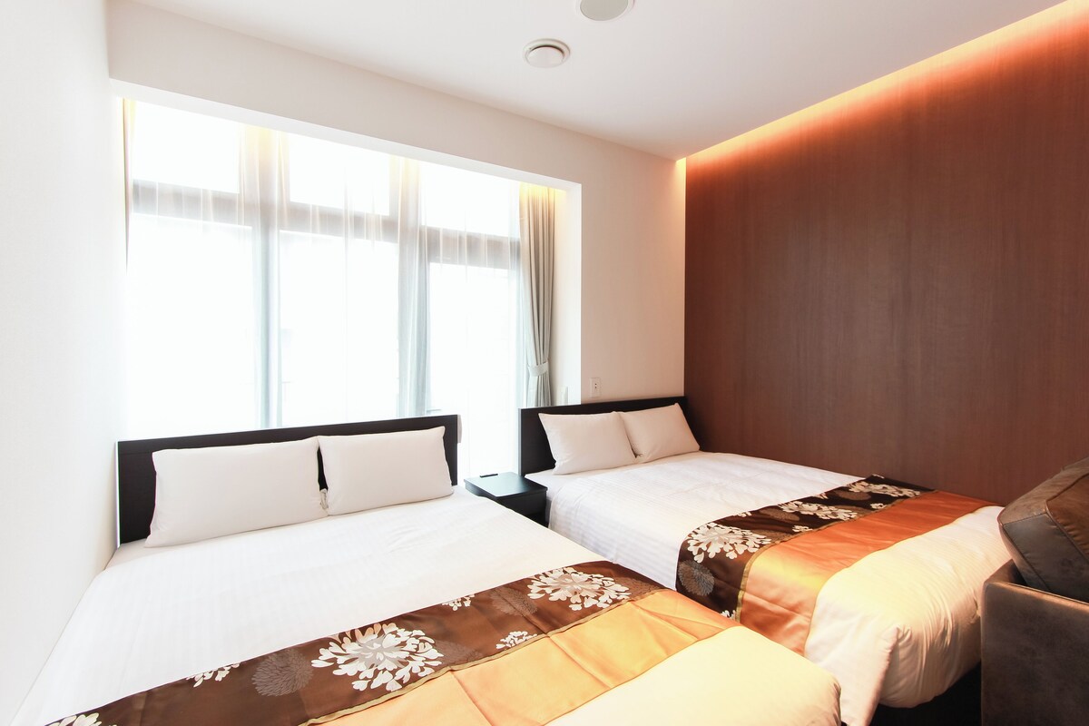 A hotel room with two beds, a wooden headboard, and a large window with curtains.