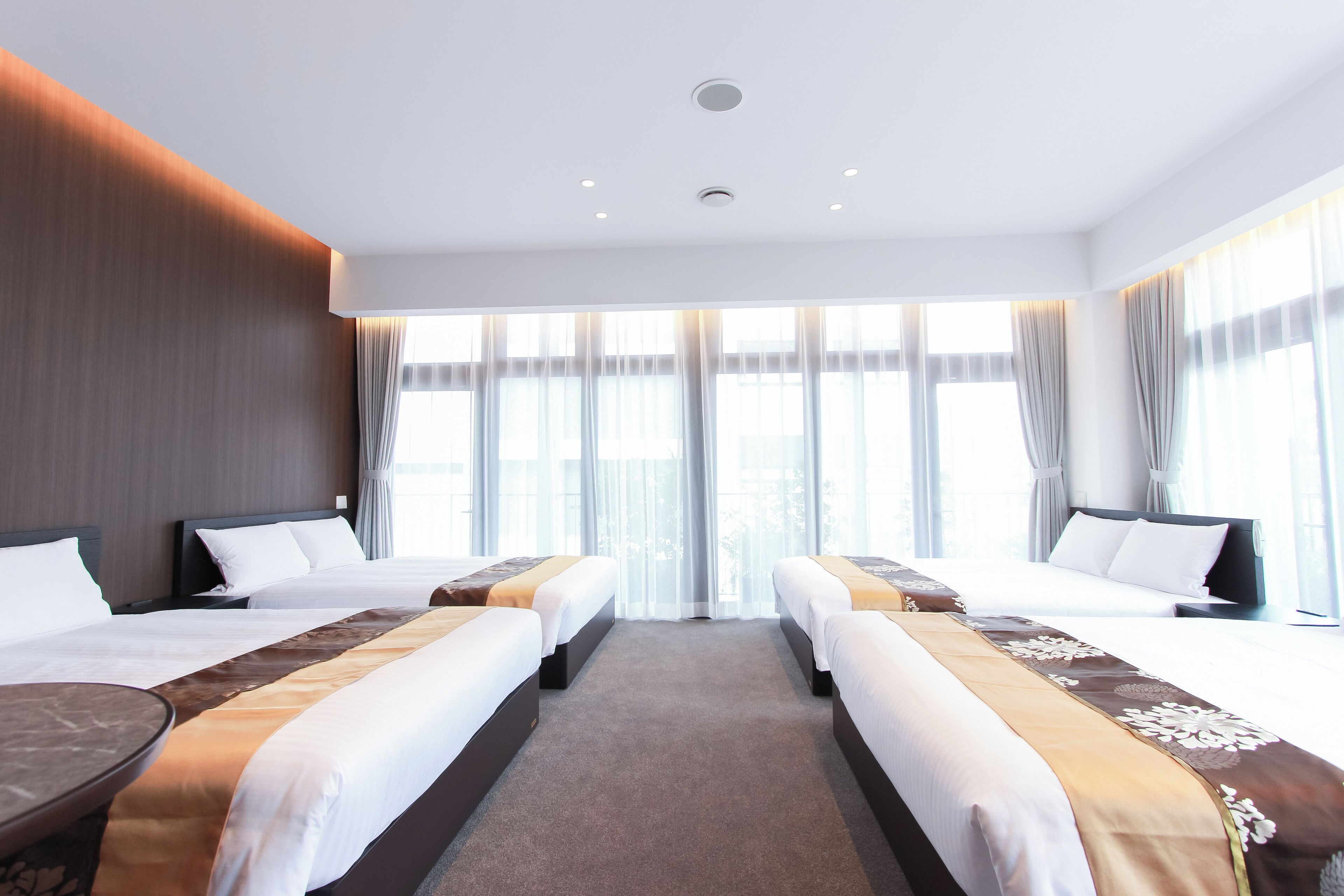 Quarto de hotel com duas camas, uma janela grande com cortinas e um teto com iluminação embutida.