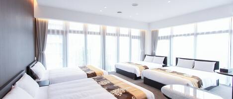 A hotel room with three beds, a small table, and large windows with curtains.