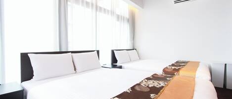 Habitación de hotel con dos camas, un ventanal con cortinas translúcidas, un aire acondicionado blanco y un corredor decorativo marrón sobre la cama.