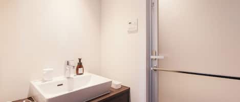 Un baño con lavamanos blanco, un secador de pelo y una botella de champú.
