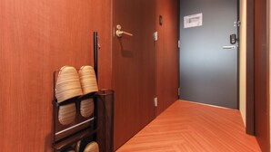 Un pasillo con paredes y suelo de madera, y una puerta con manija. A la izquierda, hay un estante con sillas dobladas.