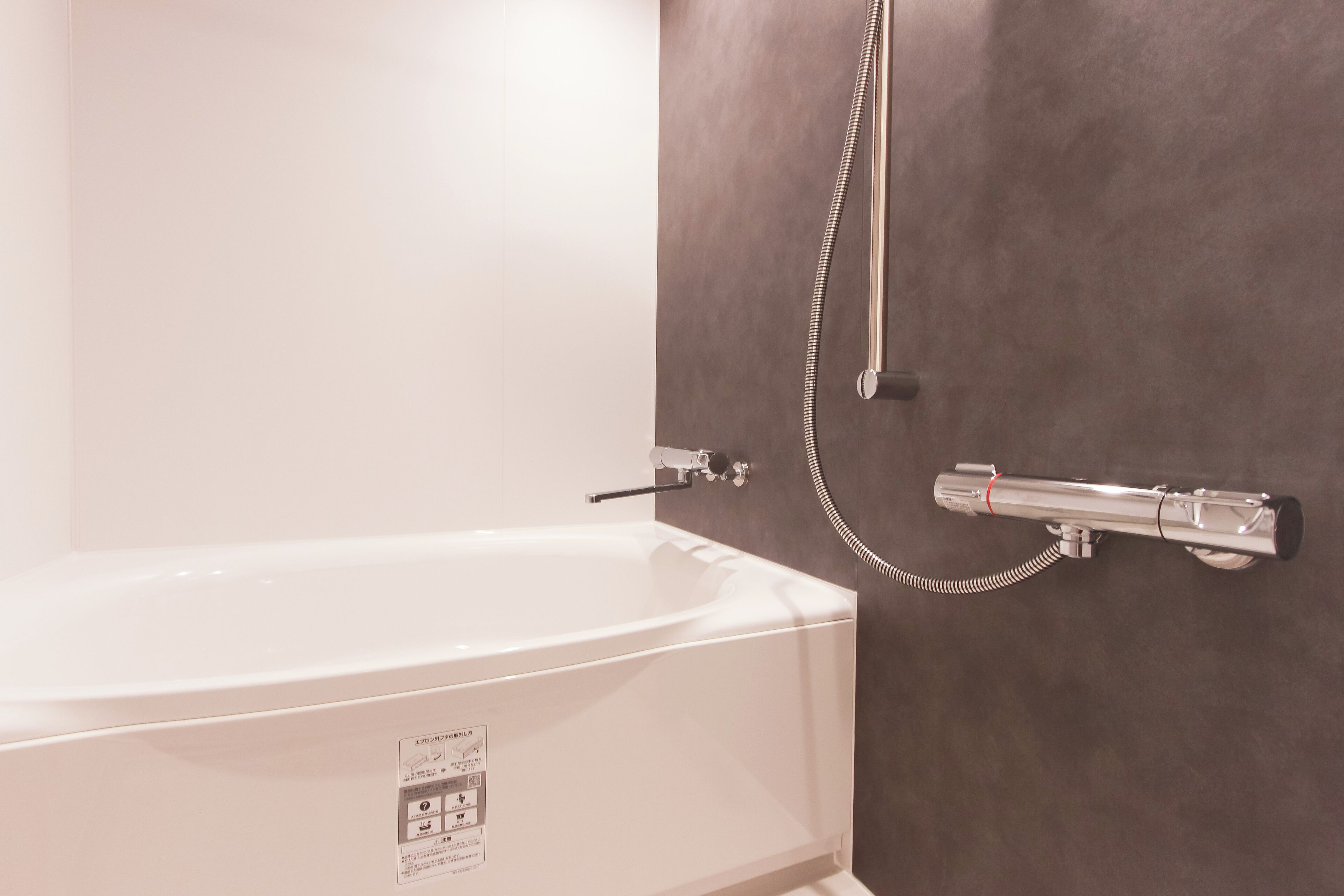 A bathroom with a white bathtub, a shower head, and a control panel.