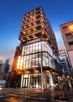 A modern building with multiple floors, large glass windows, and a prominent entrance with a blue sign. - The Arbor Hotel (Fukuoka)