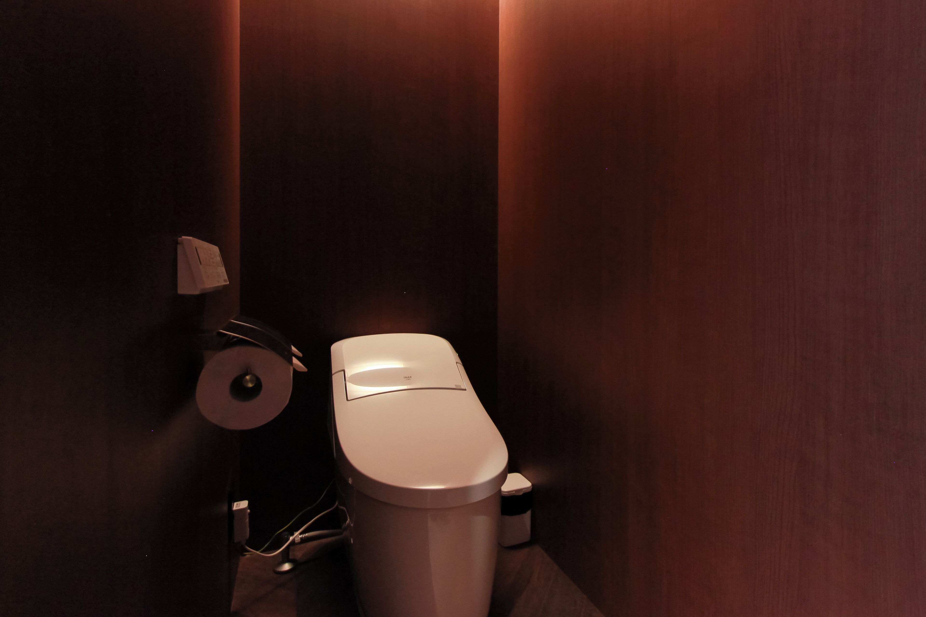Pieni, hämärästi valaistu kylpyhuone, jossa on wc, paperipyyheannostelija ja roskakori.