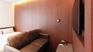 Habitación de hotel con pared de madera, un sofá marrón, un televisor de pantalla plana montado en la pared y una mesita con un control remoto.