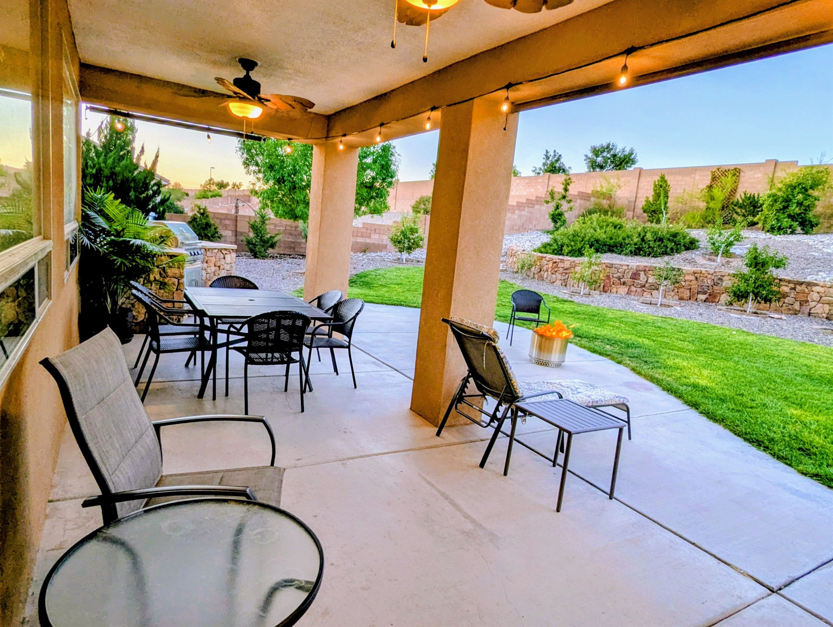 A covered patio area with a table and chairs, a ceiling fan, and string lights.