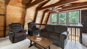 Interior acogedor de una cabaña con techo de madera, un sofá, dos sillones y una mesita.